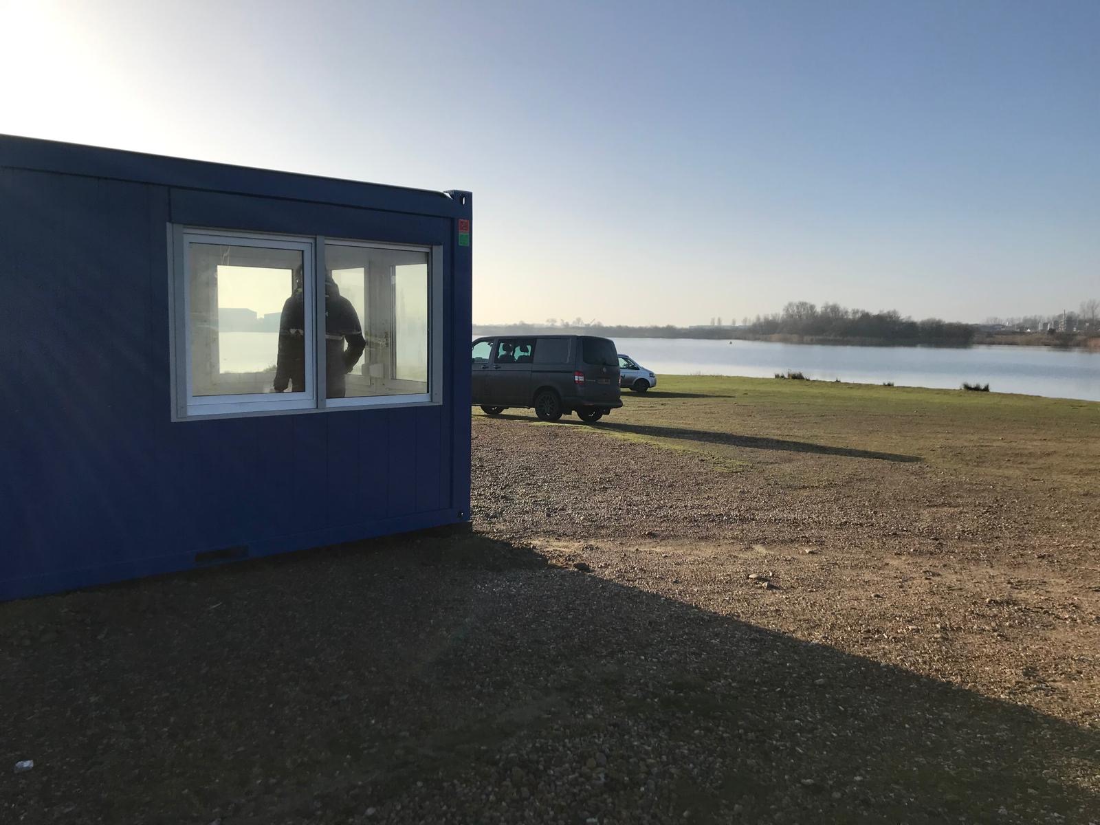 Blue modular site office cabin overlooking a lake at a watersports site