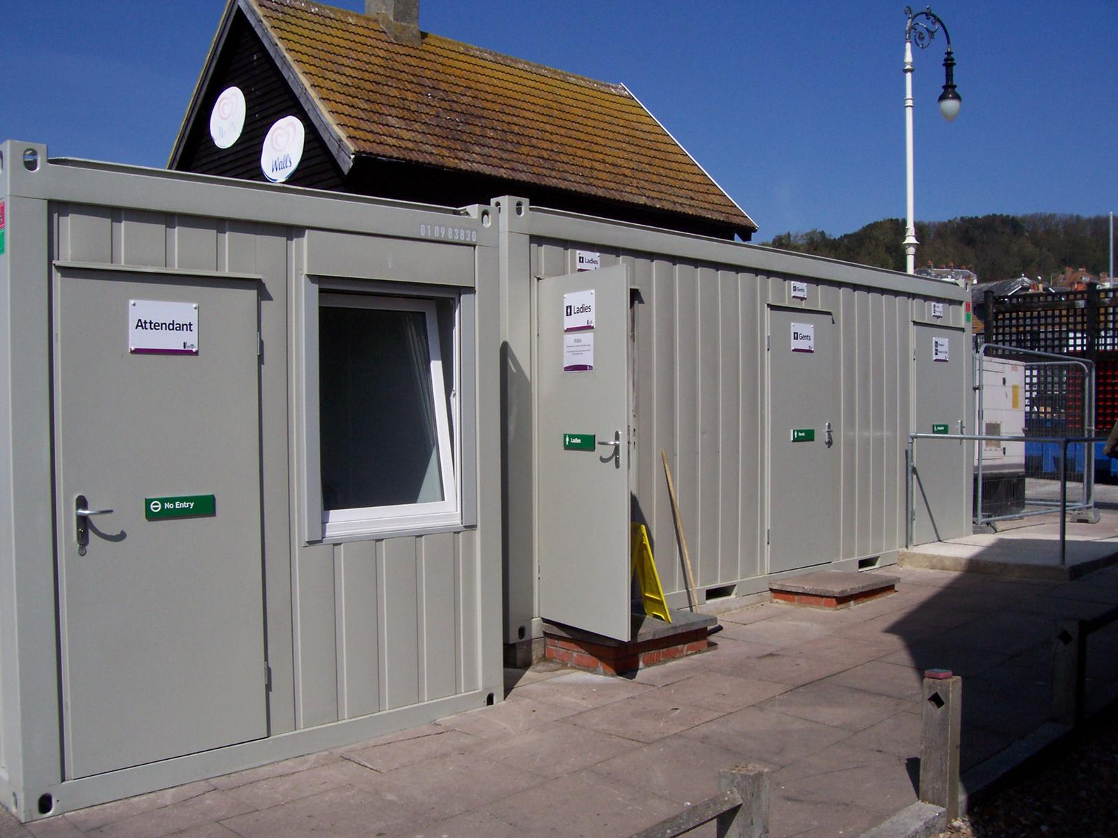 Grey modular public WC block with attendant room and signed entrances at the seafront